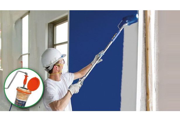 Maler mit Helm und Einwegmaske streich mit Hilfe vom JetRoller eine Wand blau