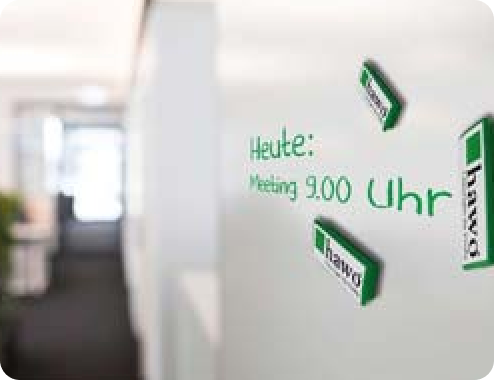Beschreibbare Magnetische Wand mit der Aufschrift: "Heute: Meeting 9.00 Uhr" und Magneten mit hawo-Logo